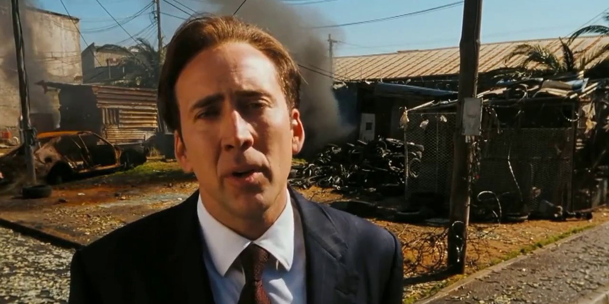 Nicolas Cage in Lord of War looking at the camera with debris behind him