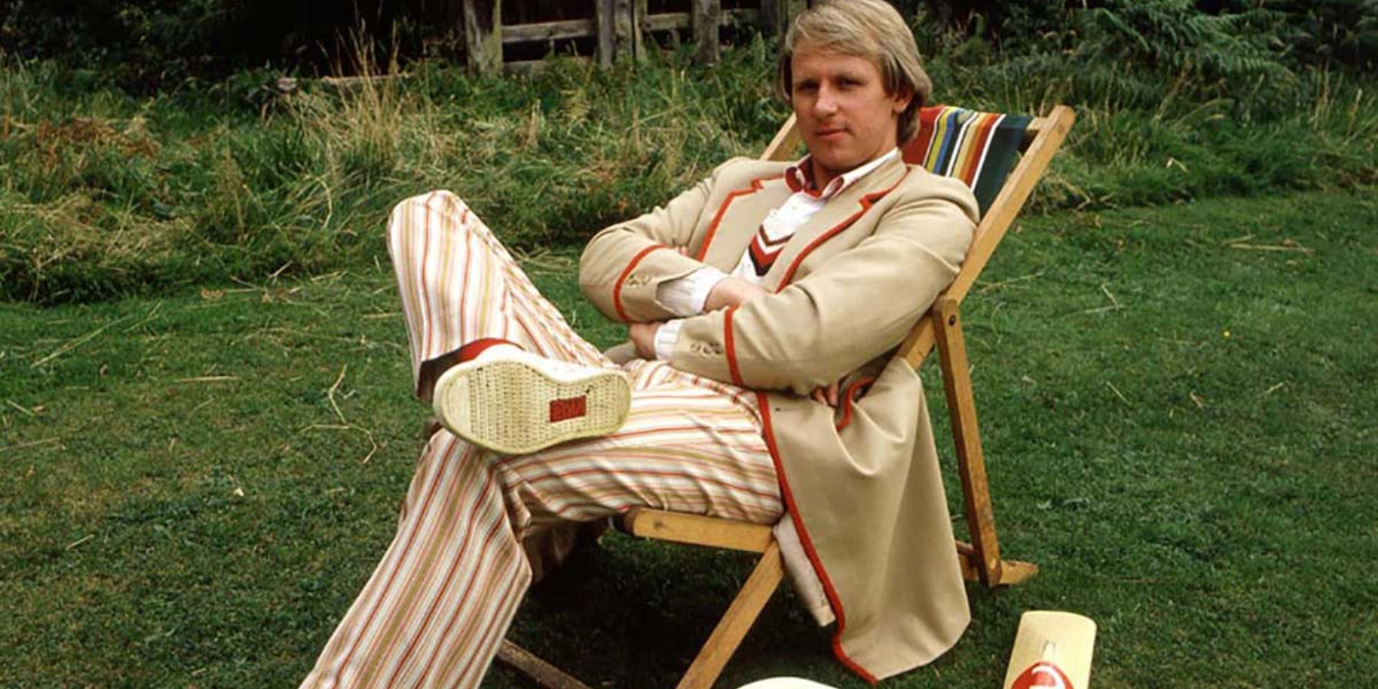 O 5º Doutor senta-se em uma cadeira de piquenique em um campo com um bastão de críquete