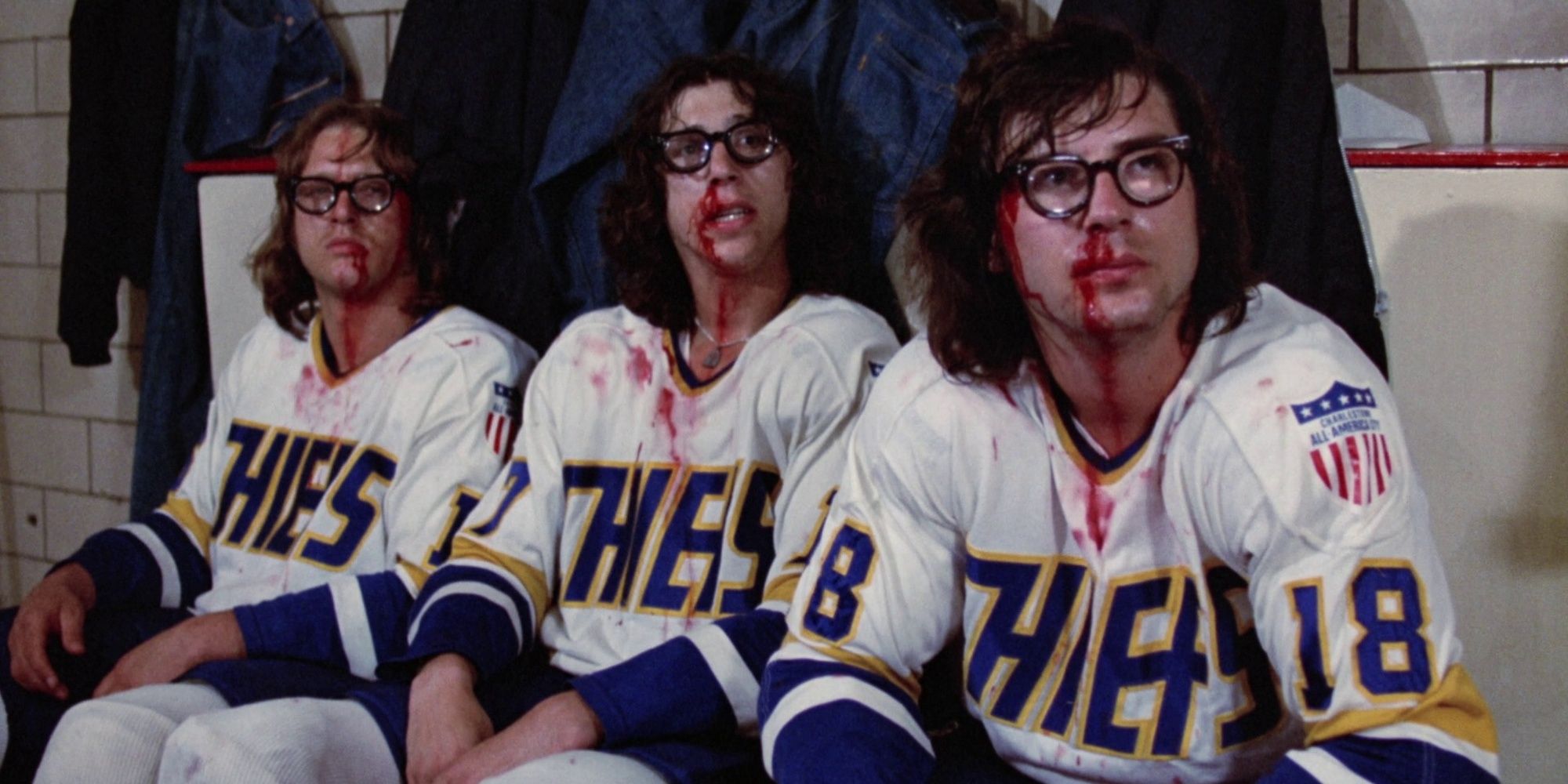 Three ice hockey players sit bloodied in their uniforms
