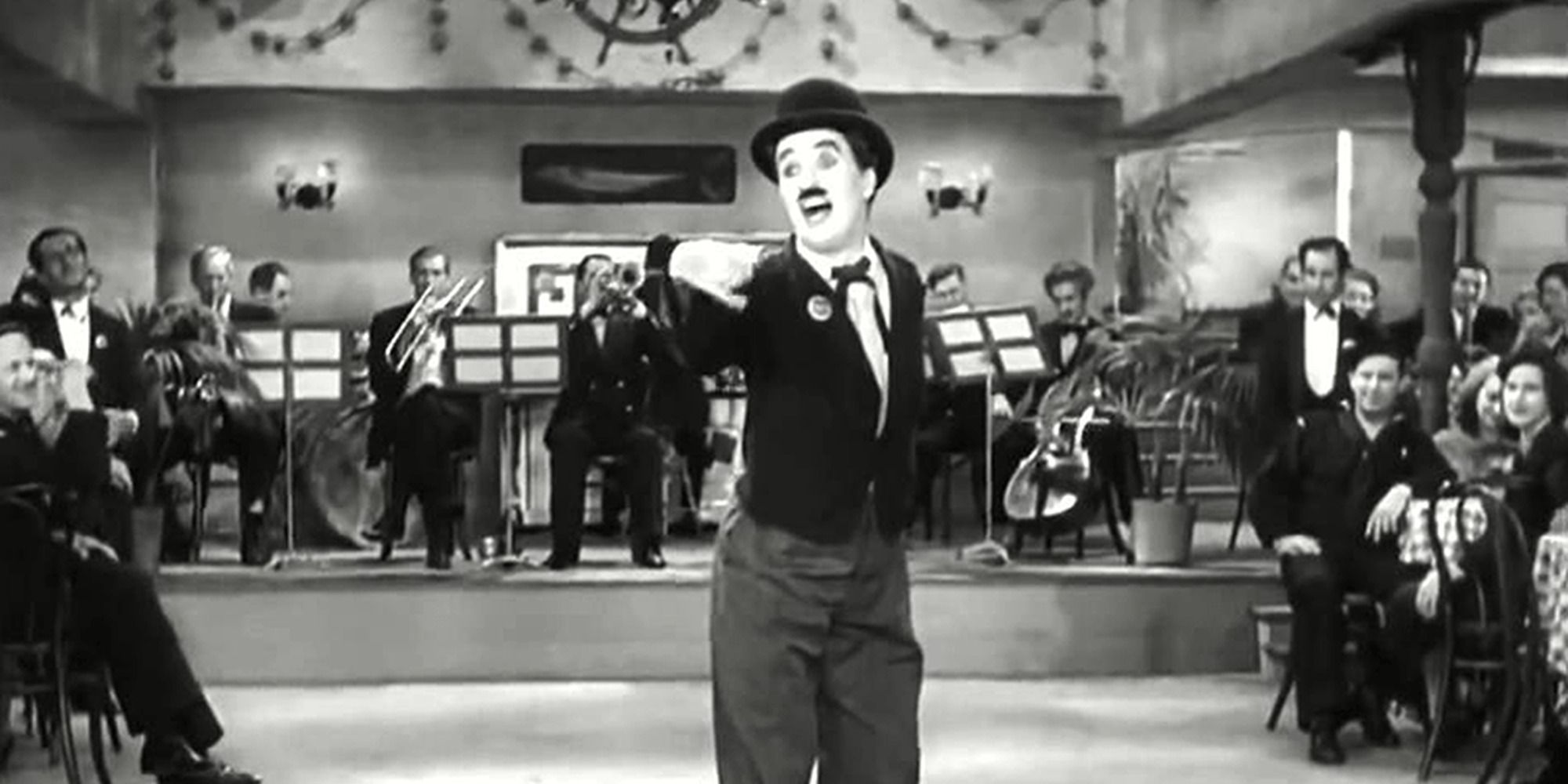 The Tramp singing a song with a band playing behind him and a crowd watching