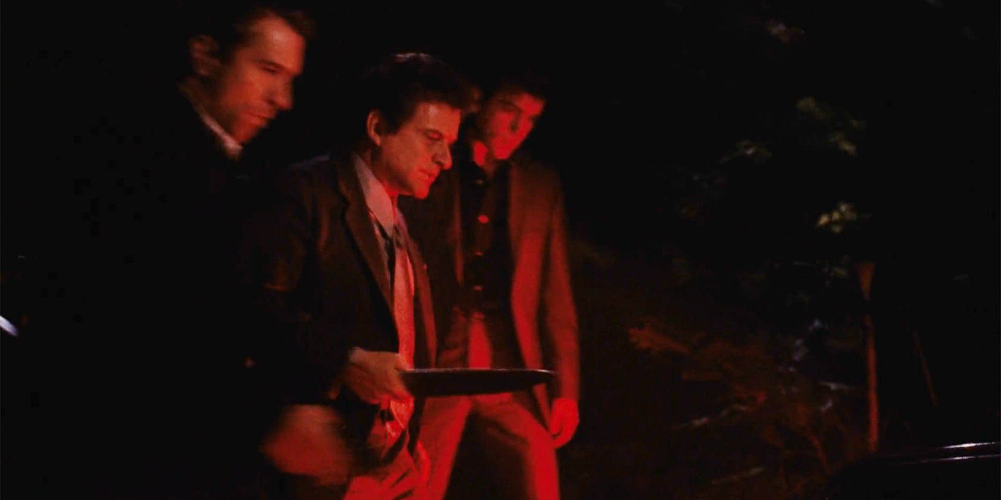 three men, one armed with a knife, looking at a car's trunk