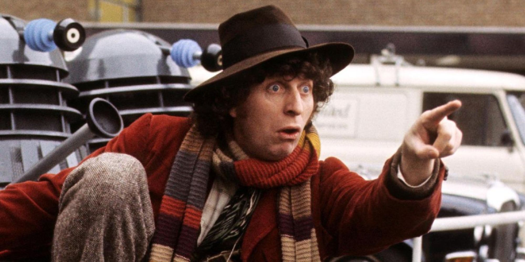 Tom Baker as the Fourth Doctor pointing while surrounded by Daleks