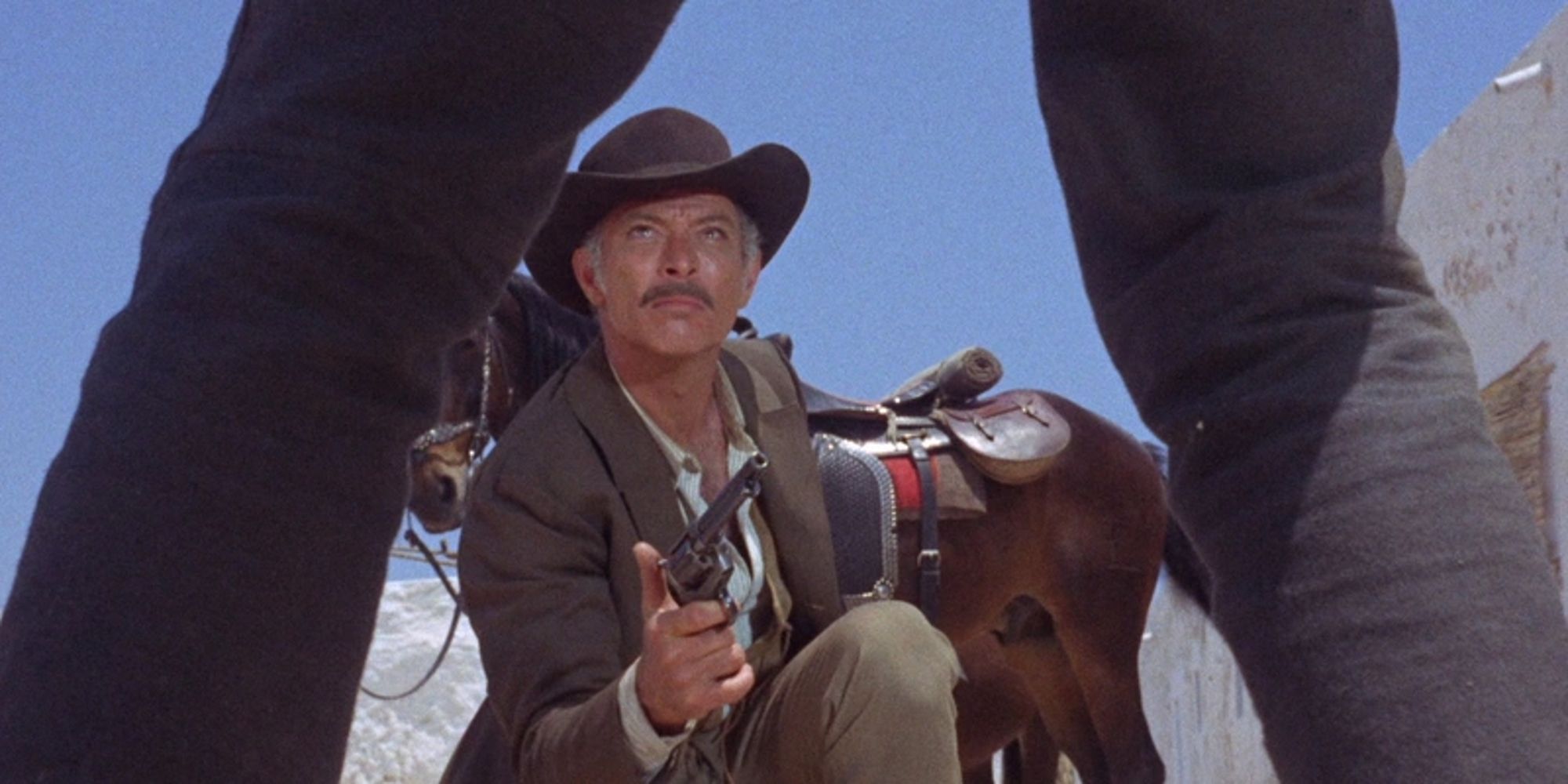 Lee Van Cleef crouches on the ground with a revolver before another man in Day of Anger