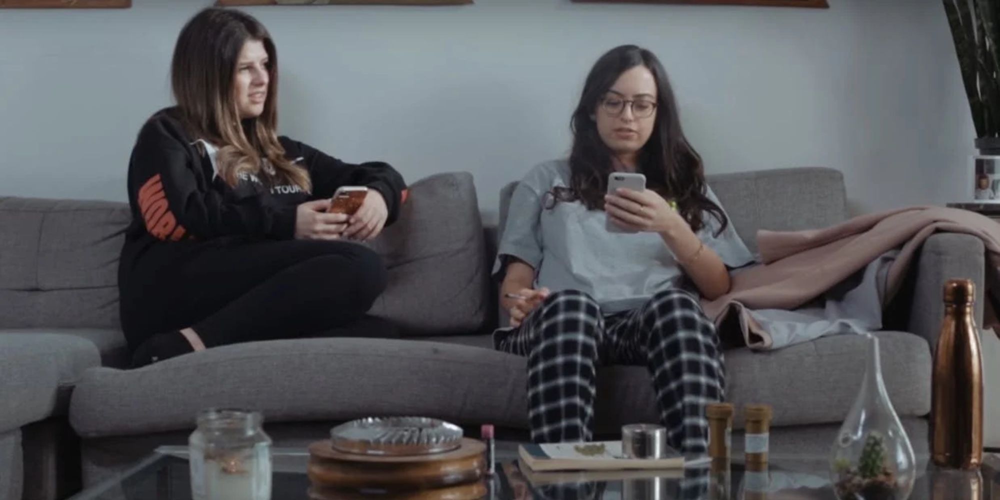 Two girls sitting on a couch, one with her phone and the other is facing the one with the phone