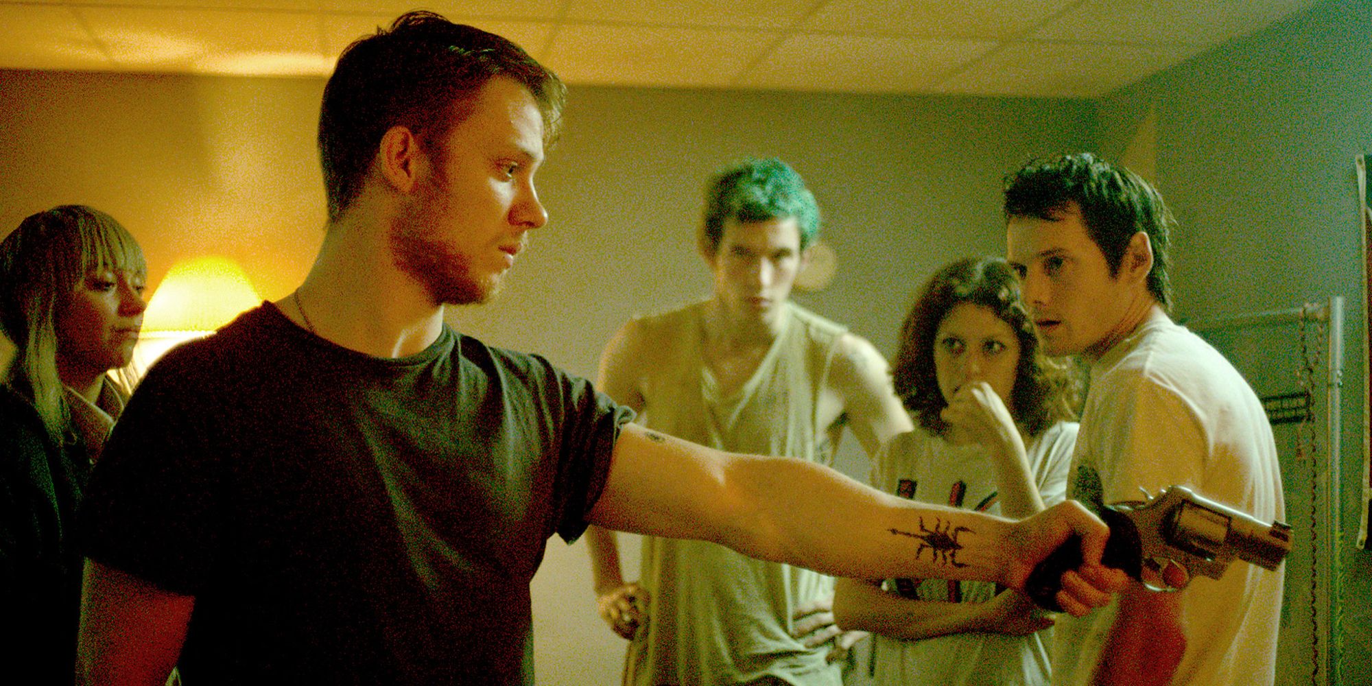 A young man aiming a gun at someone while others look from behind in Green Room