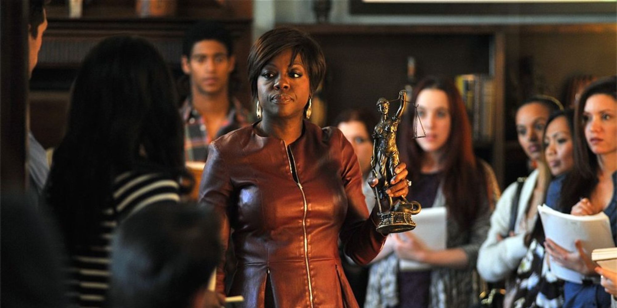 A woman holding a Lady Justice statue while surrounded with her students