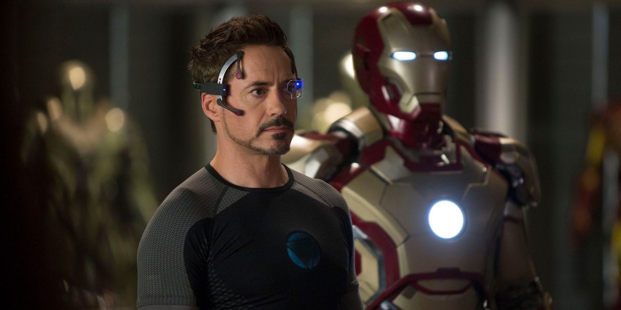 Tony Stark standing with an Iron Man suit behind him in Iron Man 3.