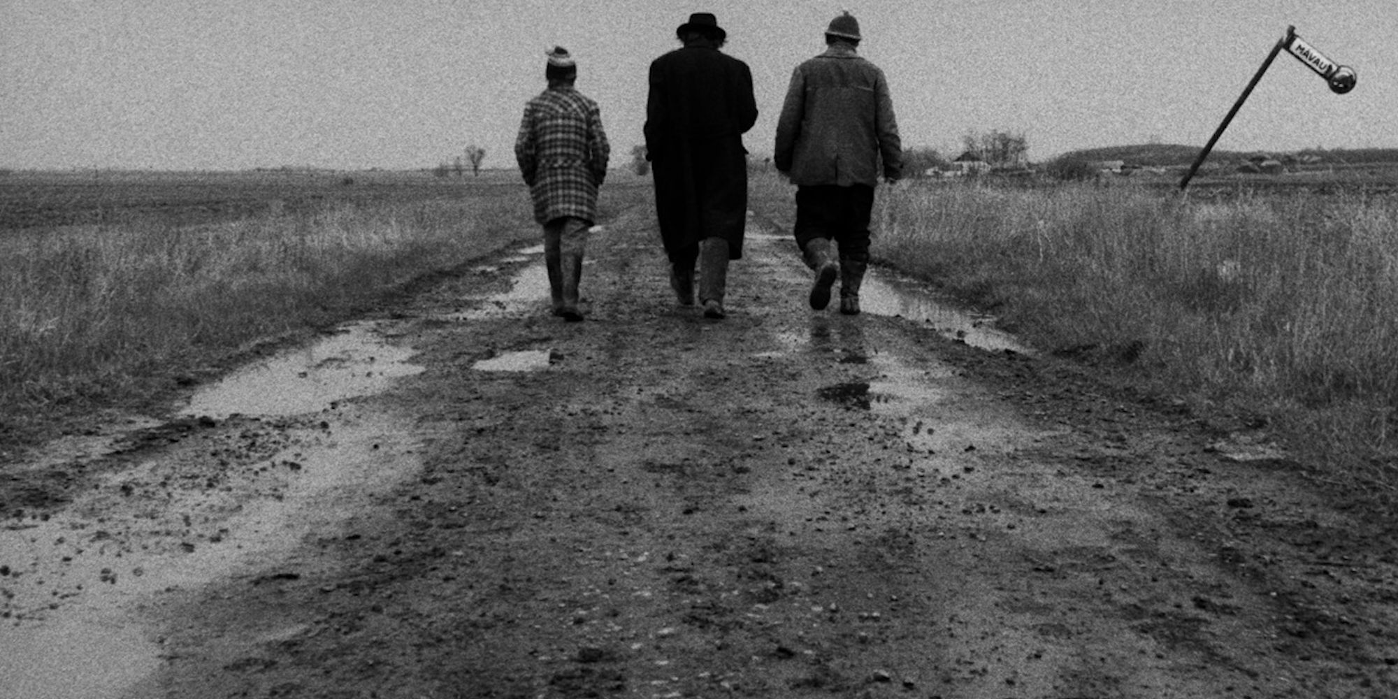 Três pessoas caminhando em uma estrada de terra em 'Satantango'