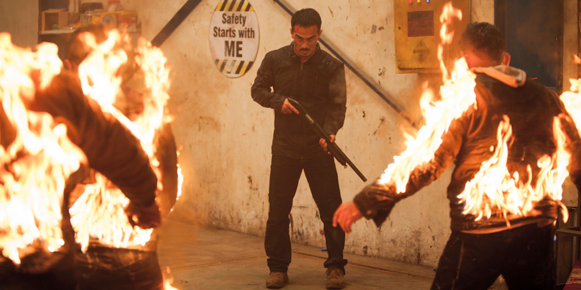 Joe Taslim with a shotgun standing in front of two men on fire in The Night Comes for Us