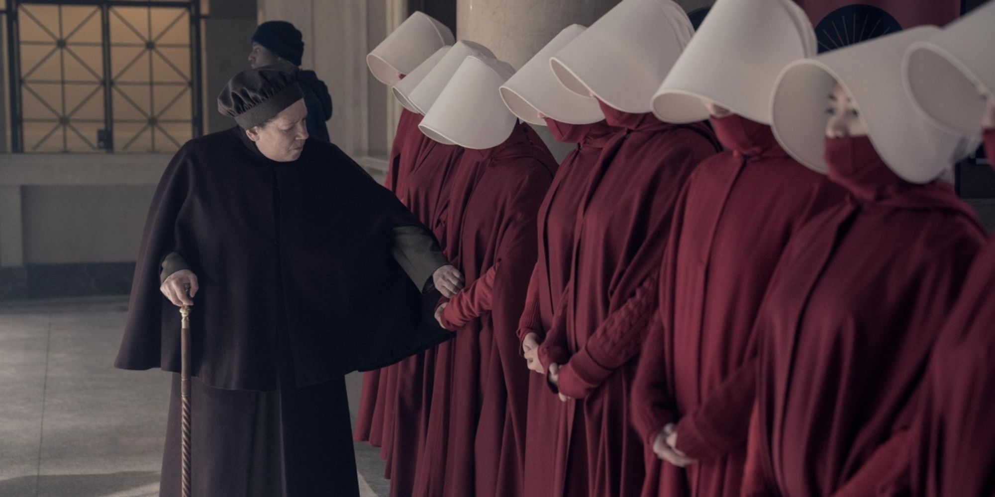 Aunt Lydia walking past a line of handmaids