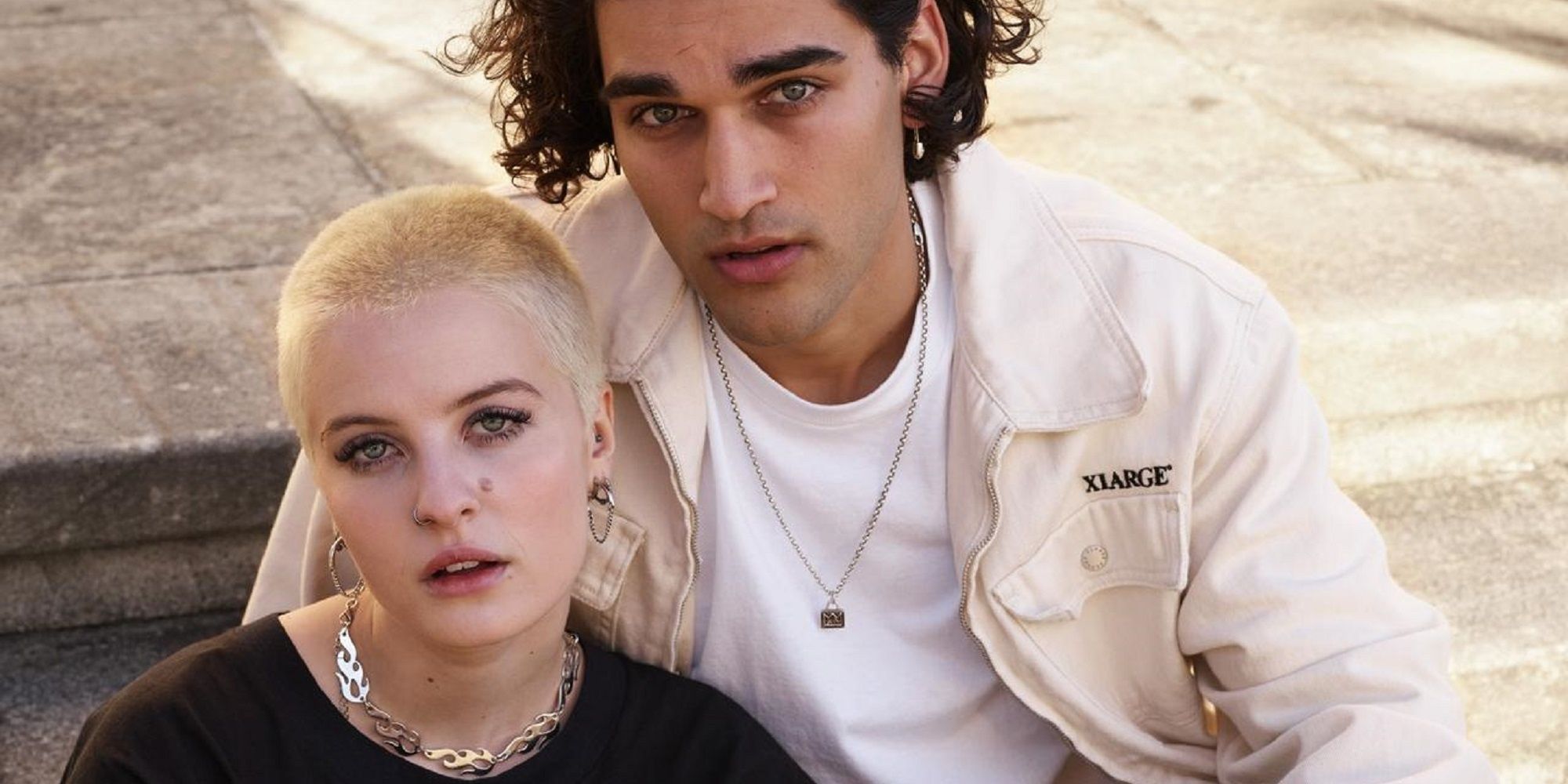 Two characters in 'Heartbreak High' sitting on the ground looking at the camera.
