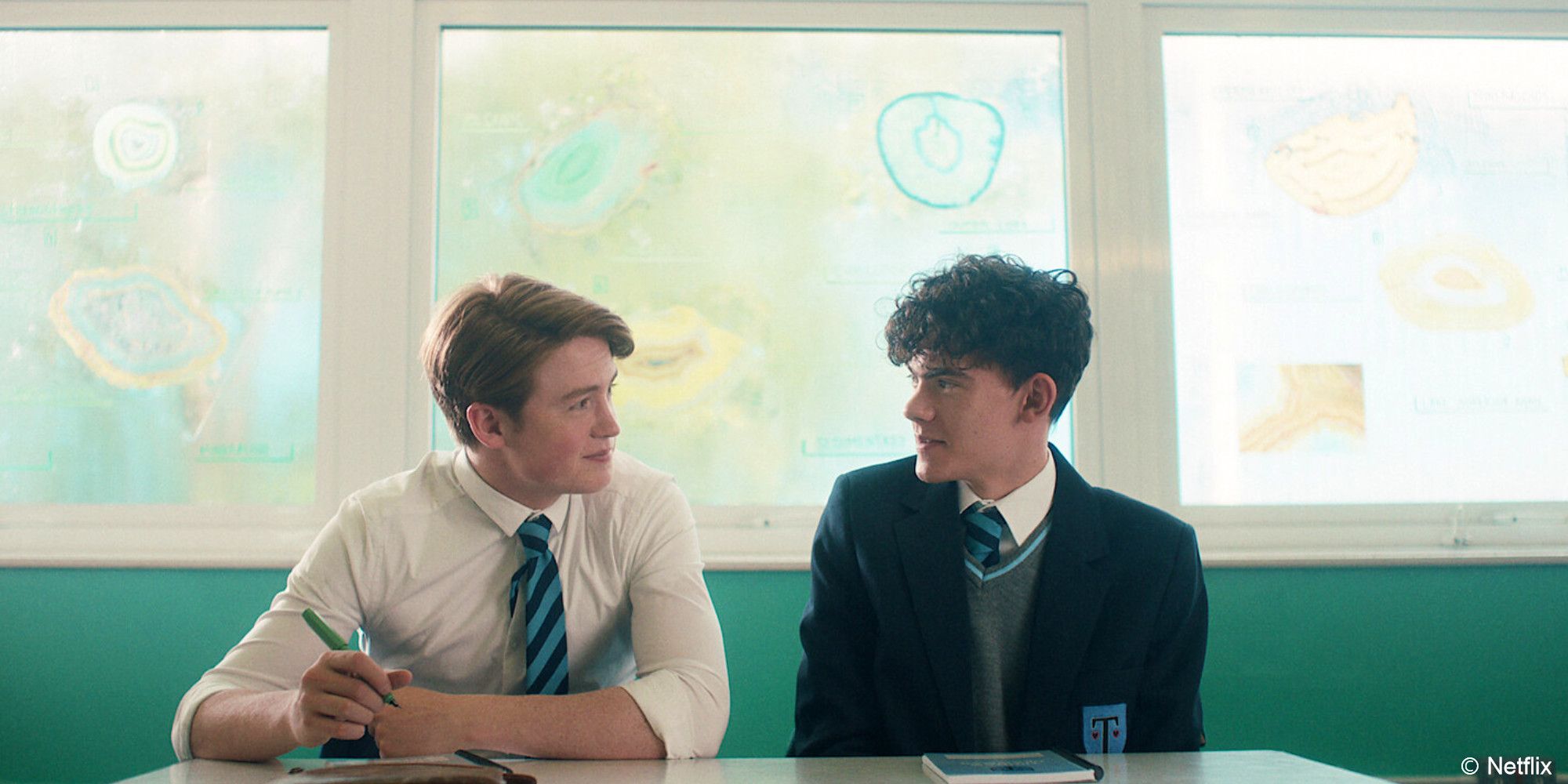 Heartstopper Charlie e Nick pareciam felizes sentados lado a lado em uma sala de aula 