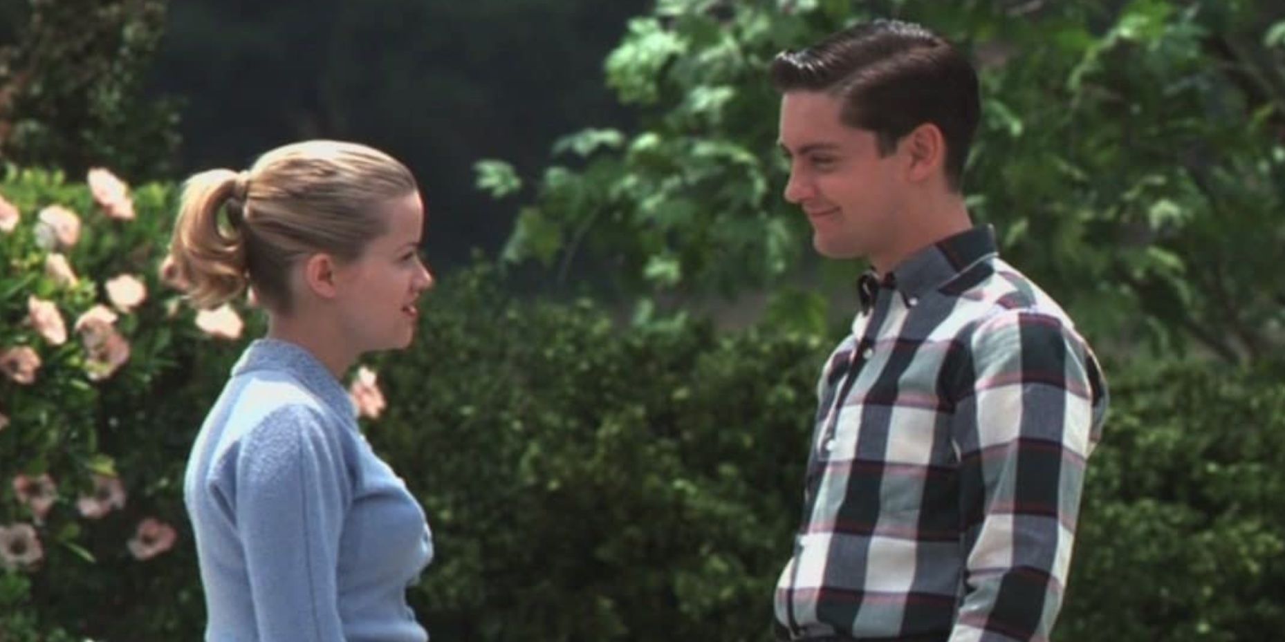 Reese Witherspoon and Tobey Maguire stand in front of flower bushes and face each other in Pleasantville.