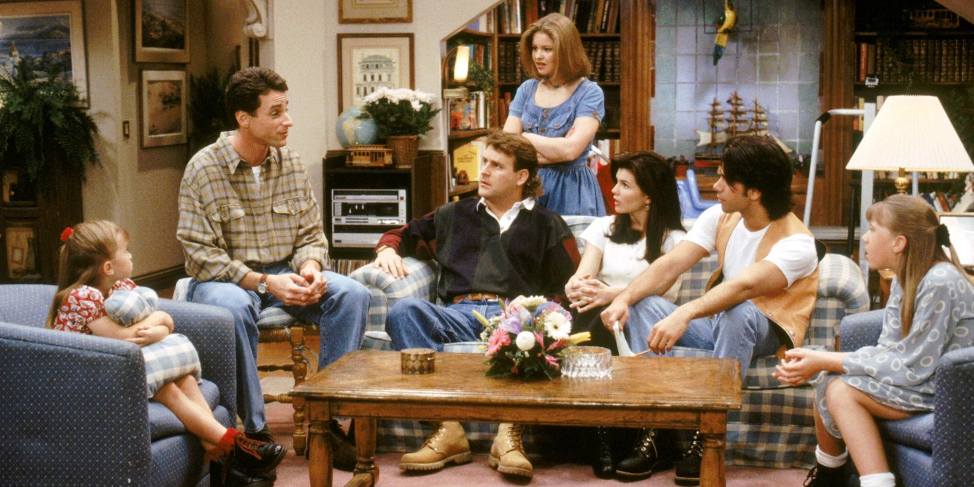 The cast of Full House all sitting together in the living room looking at Danny Tanner, played by Bob Saget, in shock 