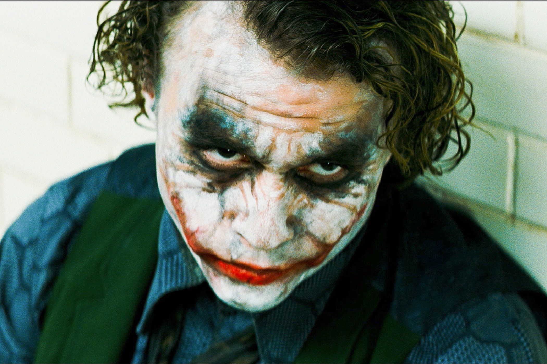 Heath Ledger as The Joker while sitting on the ground in the interrogation room in The Dark Knight.