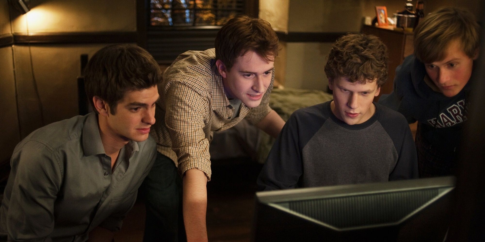 Jesse Eisenberg as Mark Zuckerberg, and his friends, surrounding a computer in The Social Network.