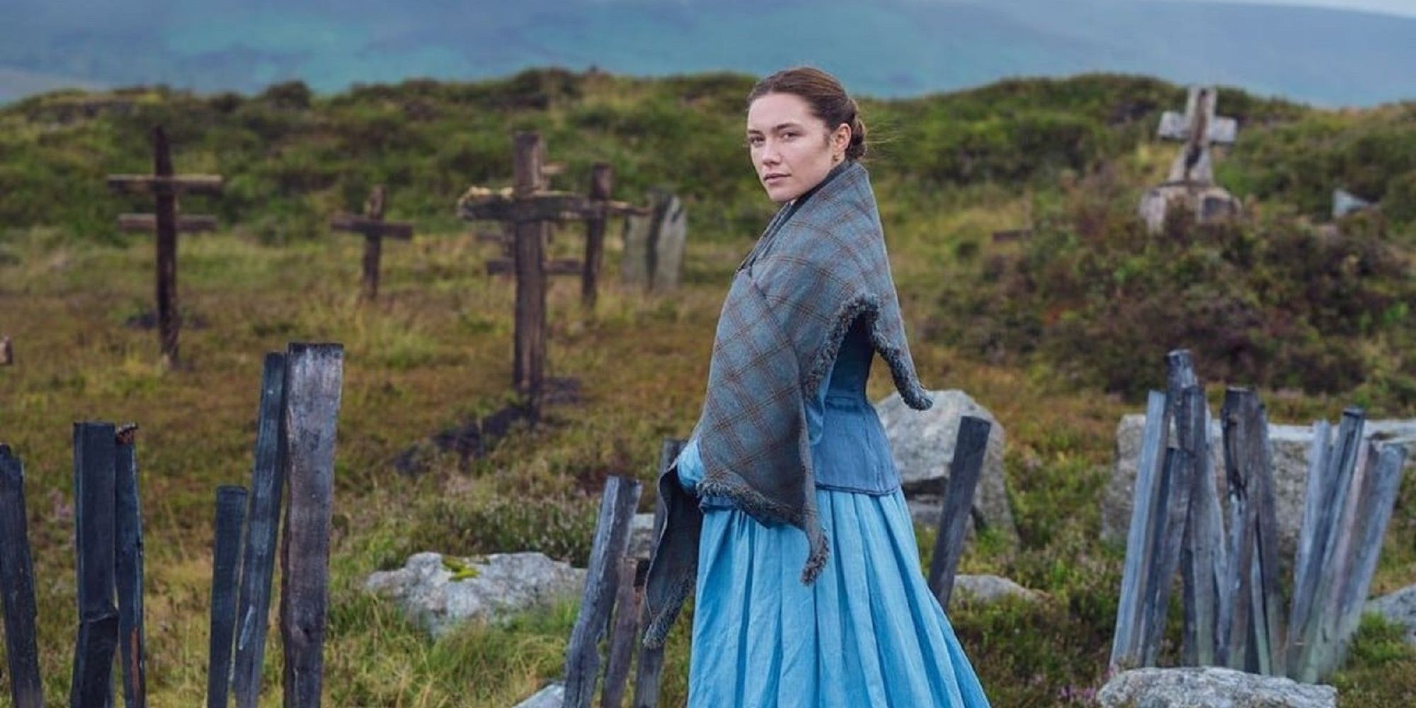 Florence Pugh as Lib, wearing a bright blue dress and standing in a graveyard in 'The Wonder.'