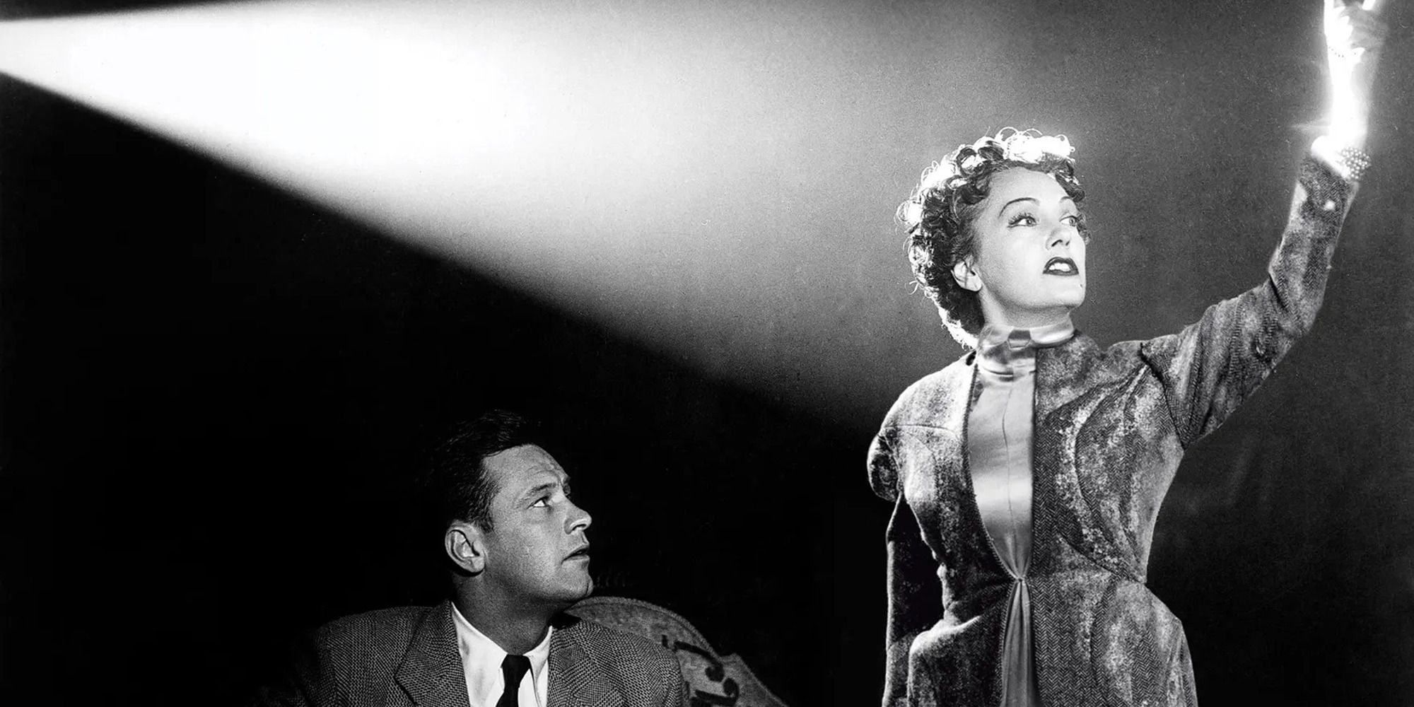 William Holden looks at Gloria Swanson who stands in a spotlight in Sunset Boulevard