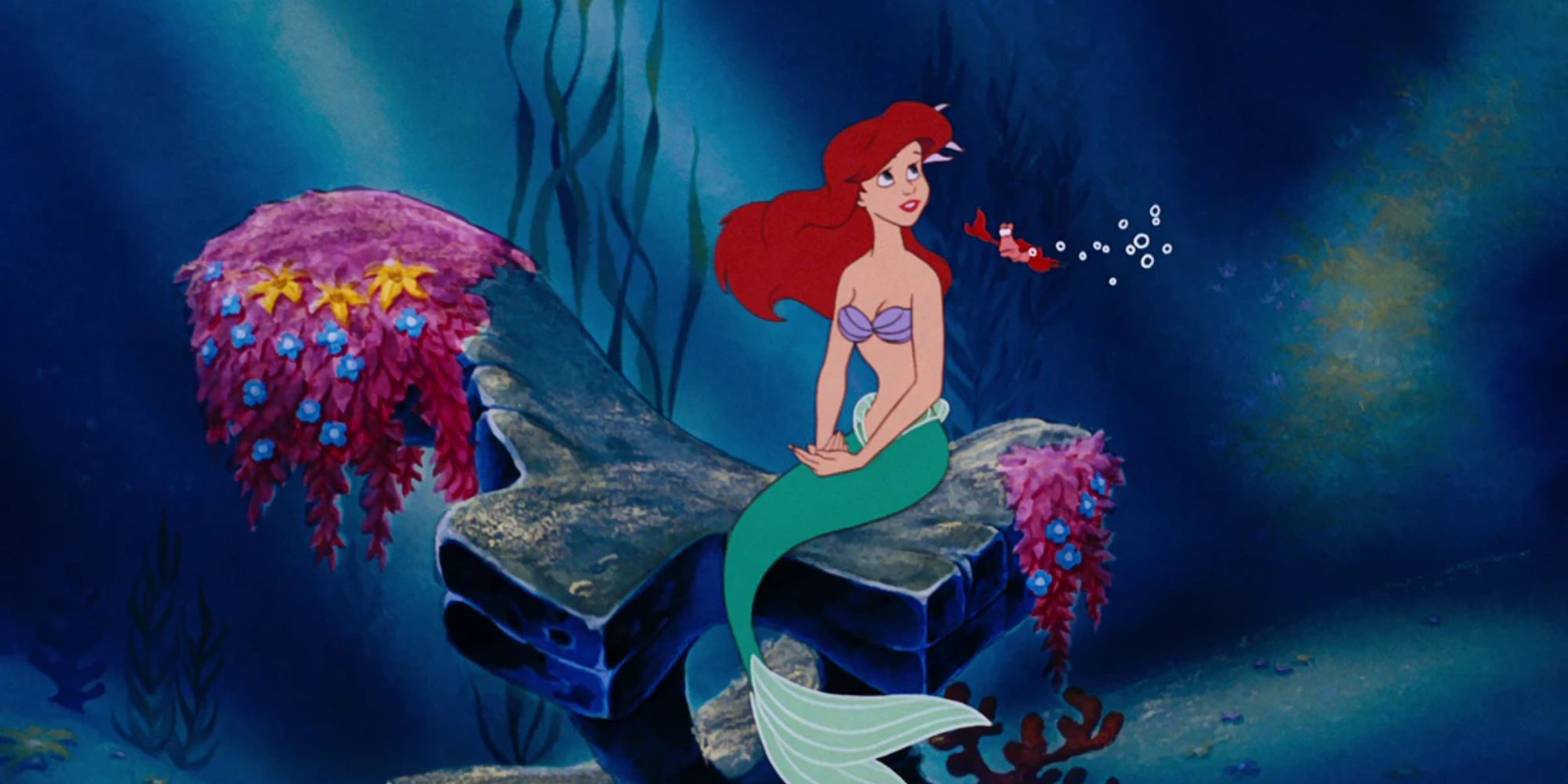 Ariel sits on an underwater rock with her crustacean friend, Sebastian in The Little Mermaid.