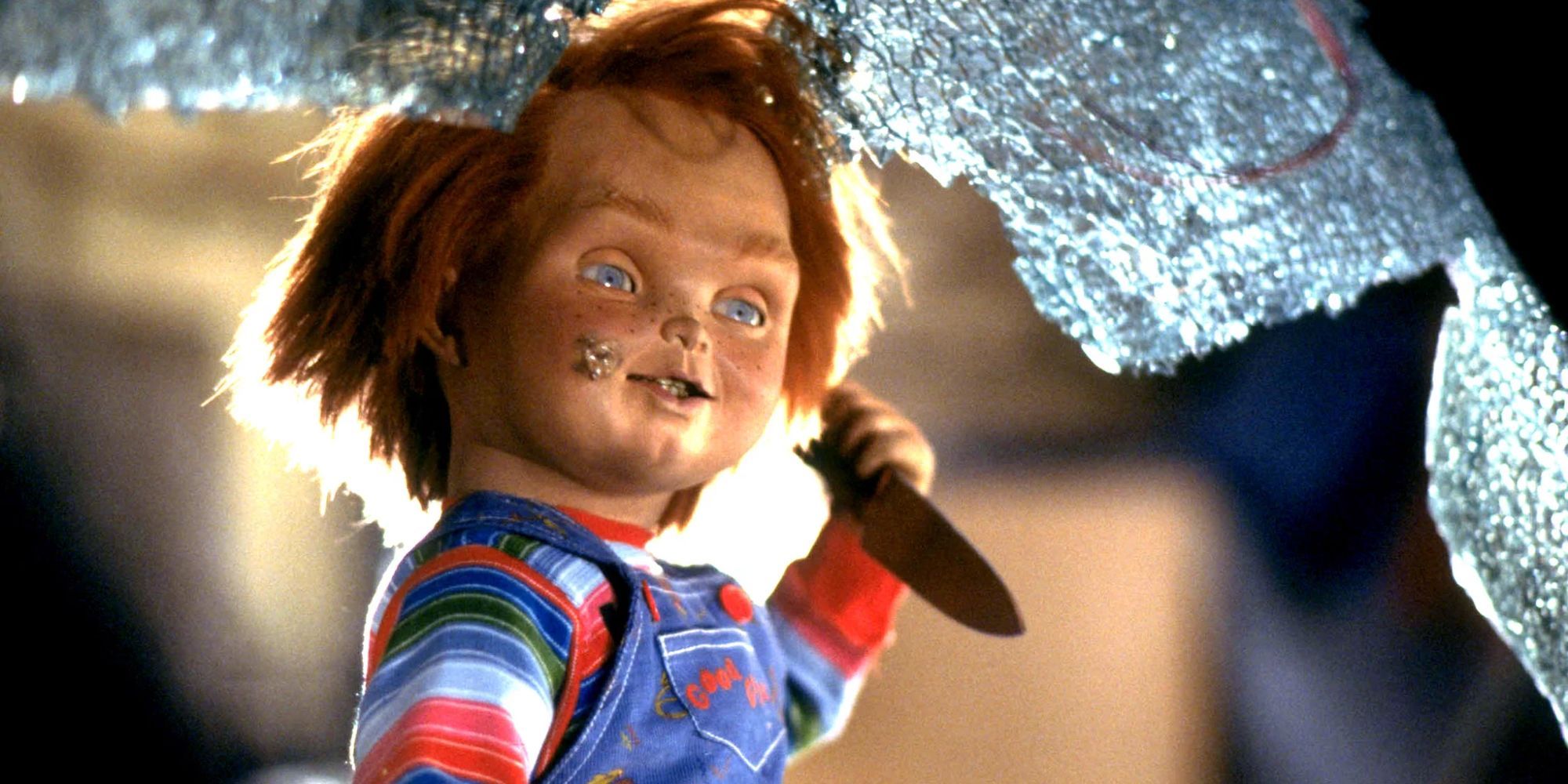 Chucky holds a knife behind a broken window