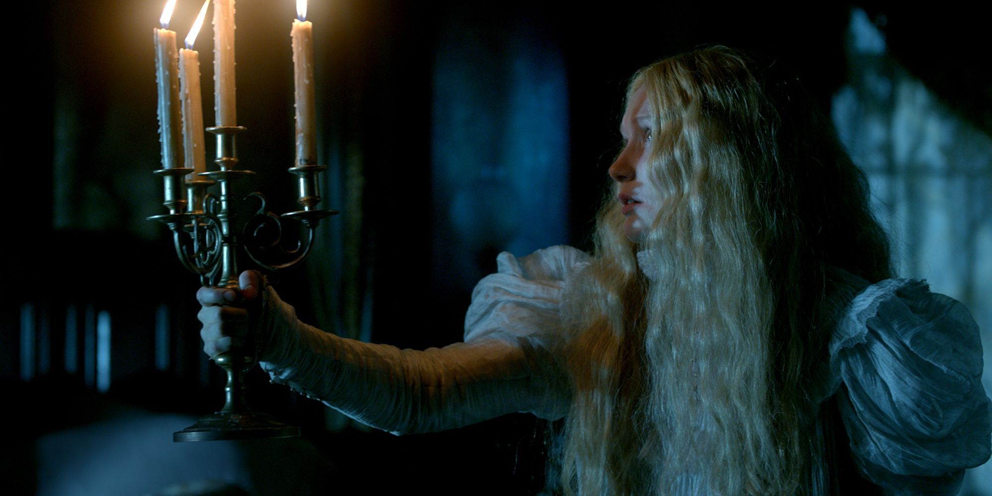 Edith searches the gloom of Crimson Peak with a candelabra