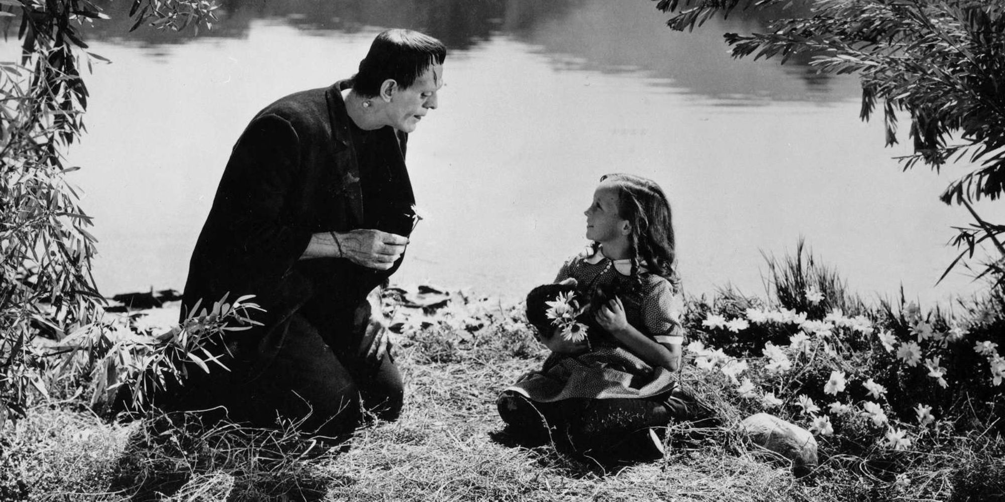 A little girl sits by a creature by the river in Frankenstein