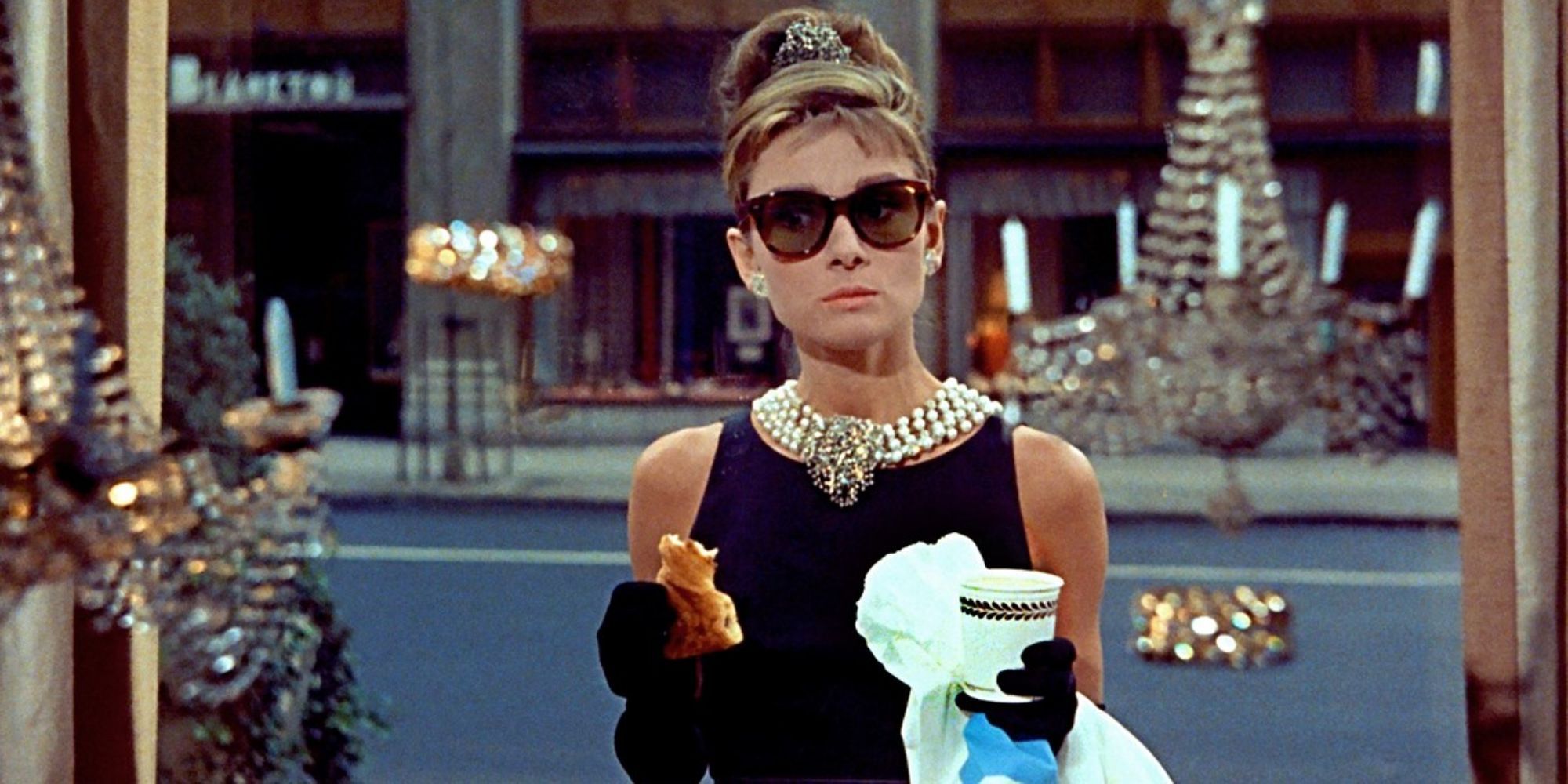 Audrey Hepburn as Holly Golightly holding a bagle and a cup of coffee in Breakfast at Tiffany's