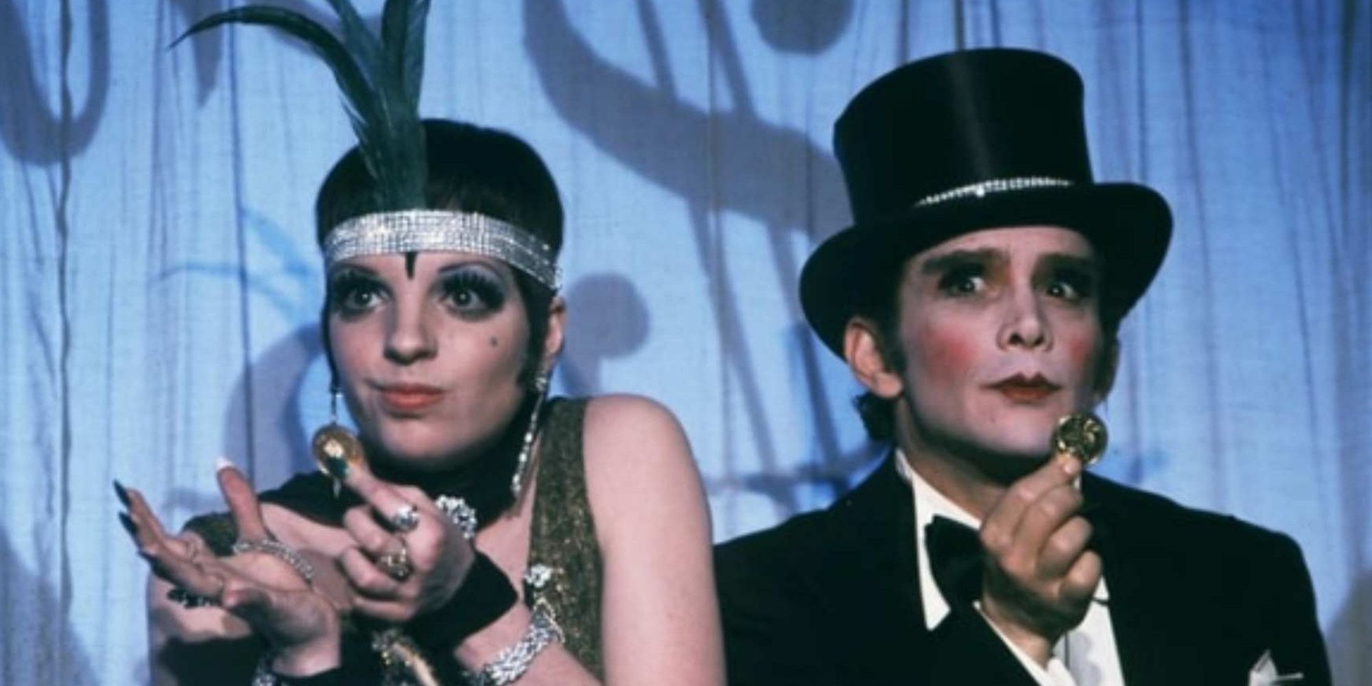 a female and male cabaret performers in full costume and makeup, in front of a blue curtain