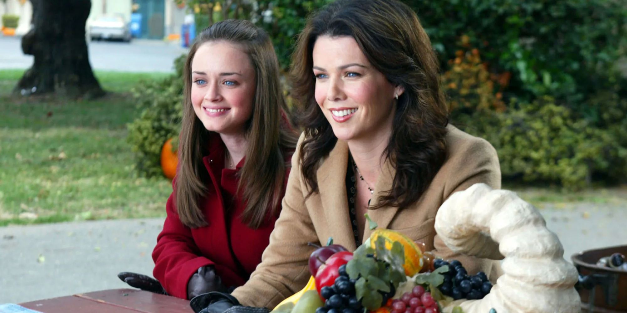 Lauren Graham and Alexis Bledel as Lorelai and Rory Gilmore, sitting at a picnic table smiling on Gilmore Girls