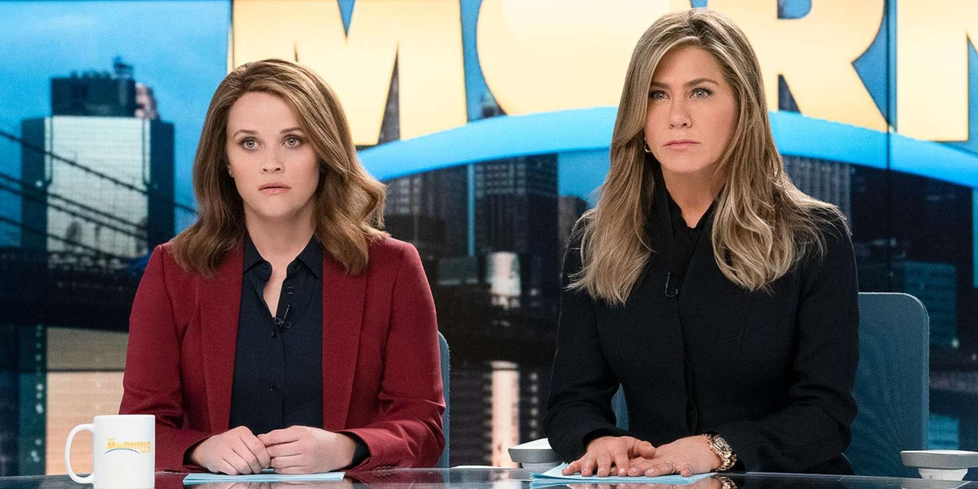Reese Witherspoon and Jennifer Aniston sitting at their desk looking confused in The Morning Show