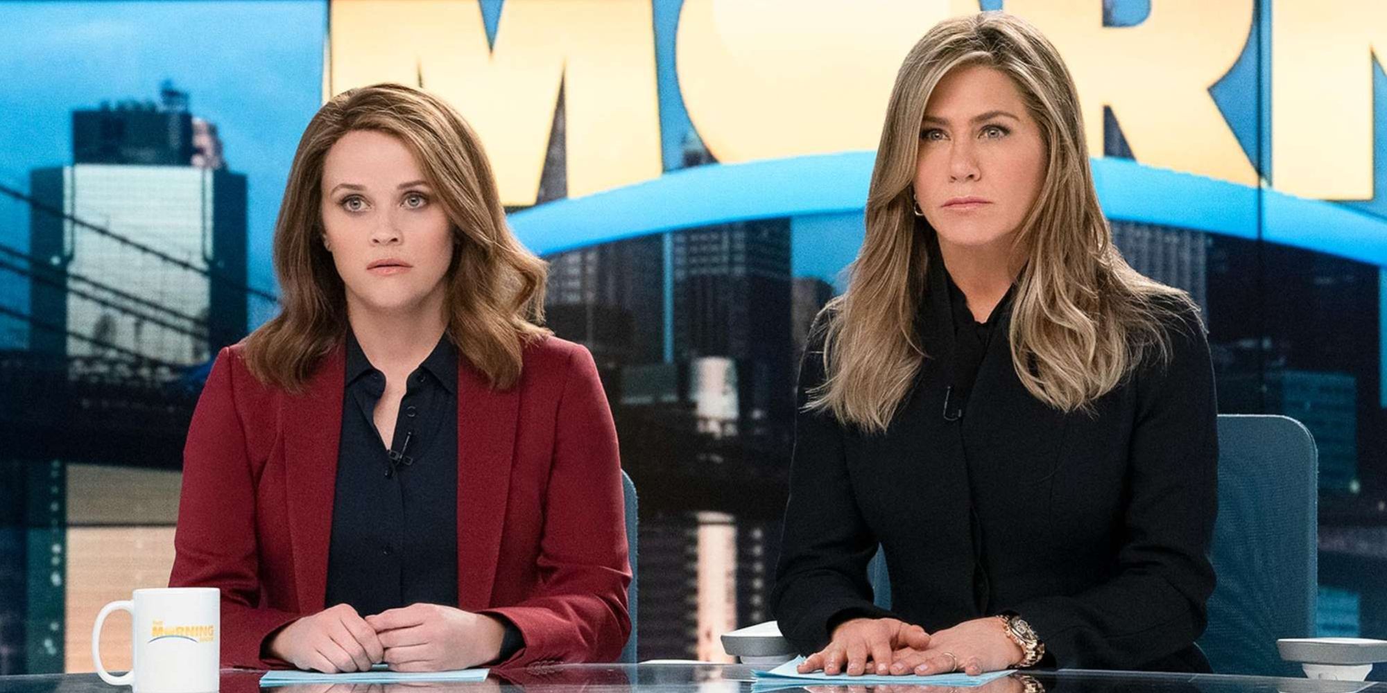 Reese Witherspoon and Jennifer Aniston sitting at their desk looking confused 