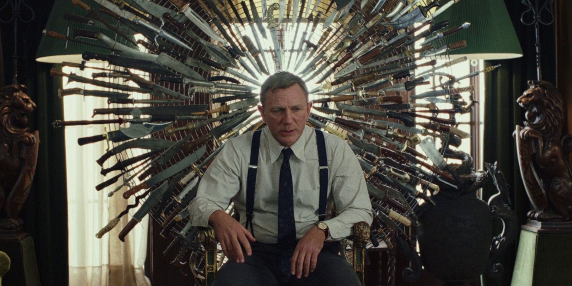 Daniel Craig sitting in a chair in front of a wheel of knives