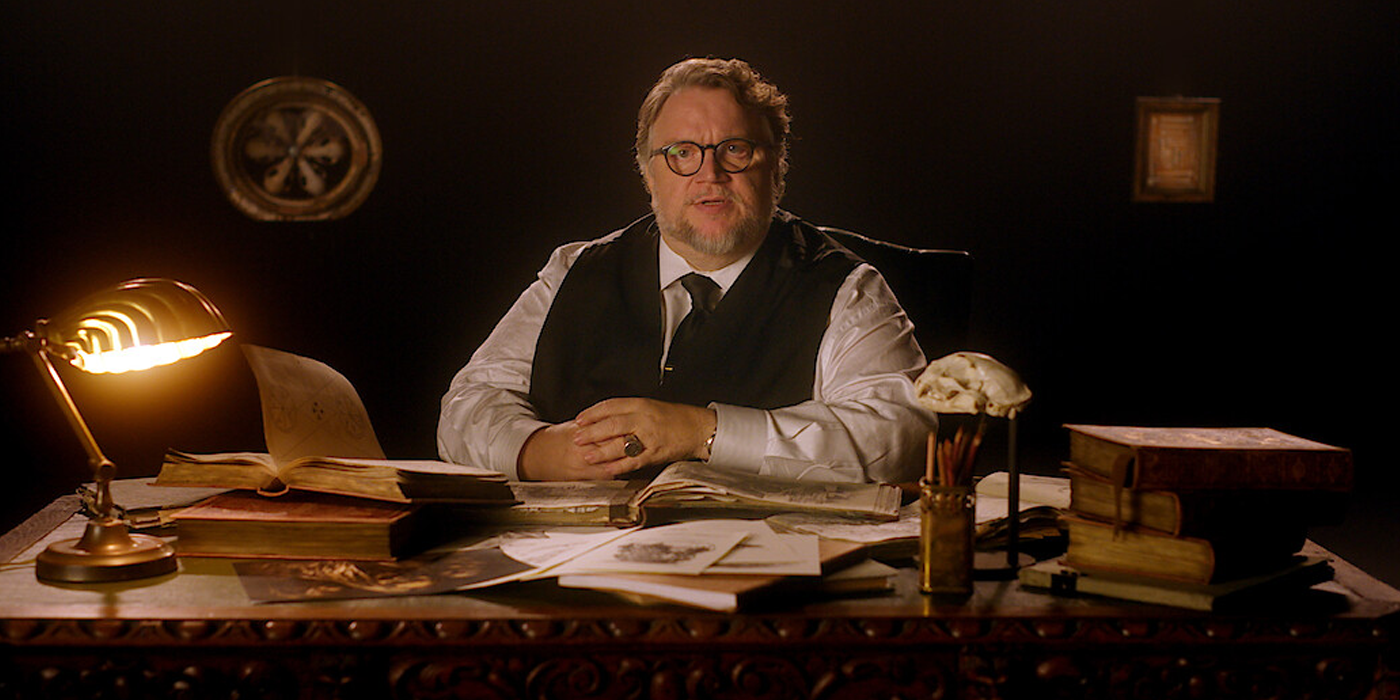 Guillermo del Toro está sentado atrás de uma mesa e fala para a câmera.