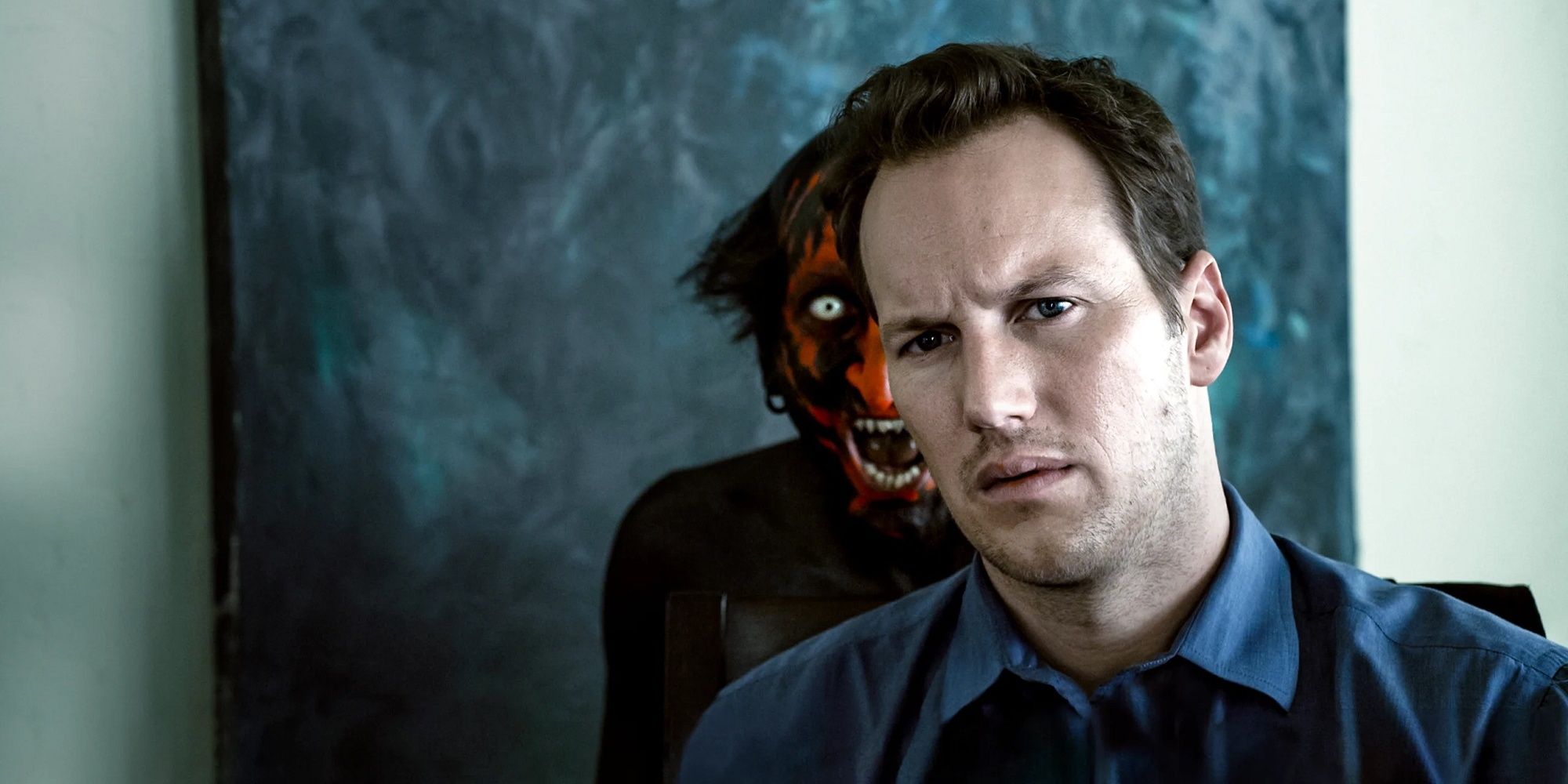 Patrick Wilson dans le rôle de Josh assis à la table de la cuisine avec le démon au visage rouge à lèvres qui surgit derrière lui dans 'Insidious'.