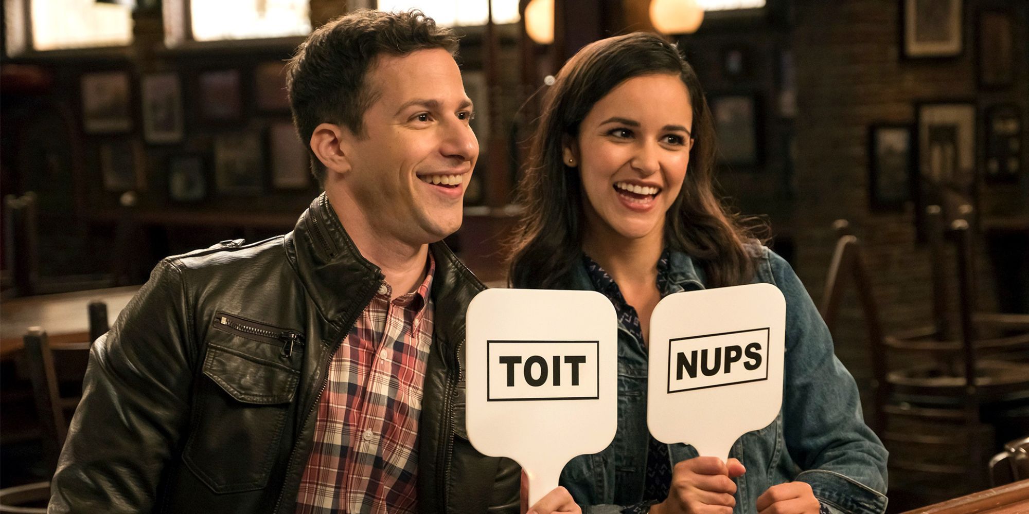 Jake and Amy smiling while holding signs in Brooklyn Nine-Nine.
