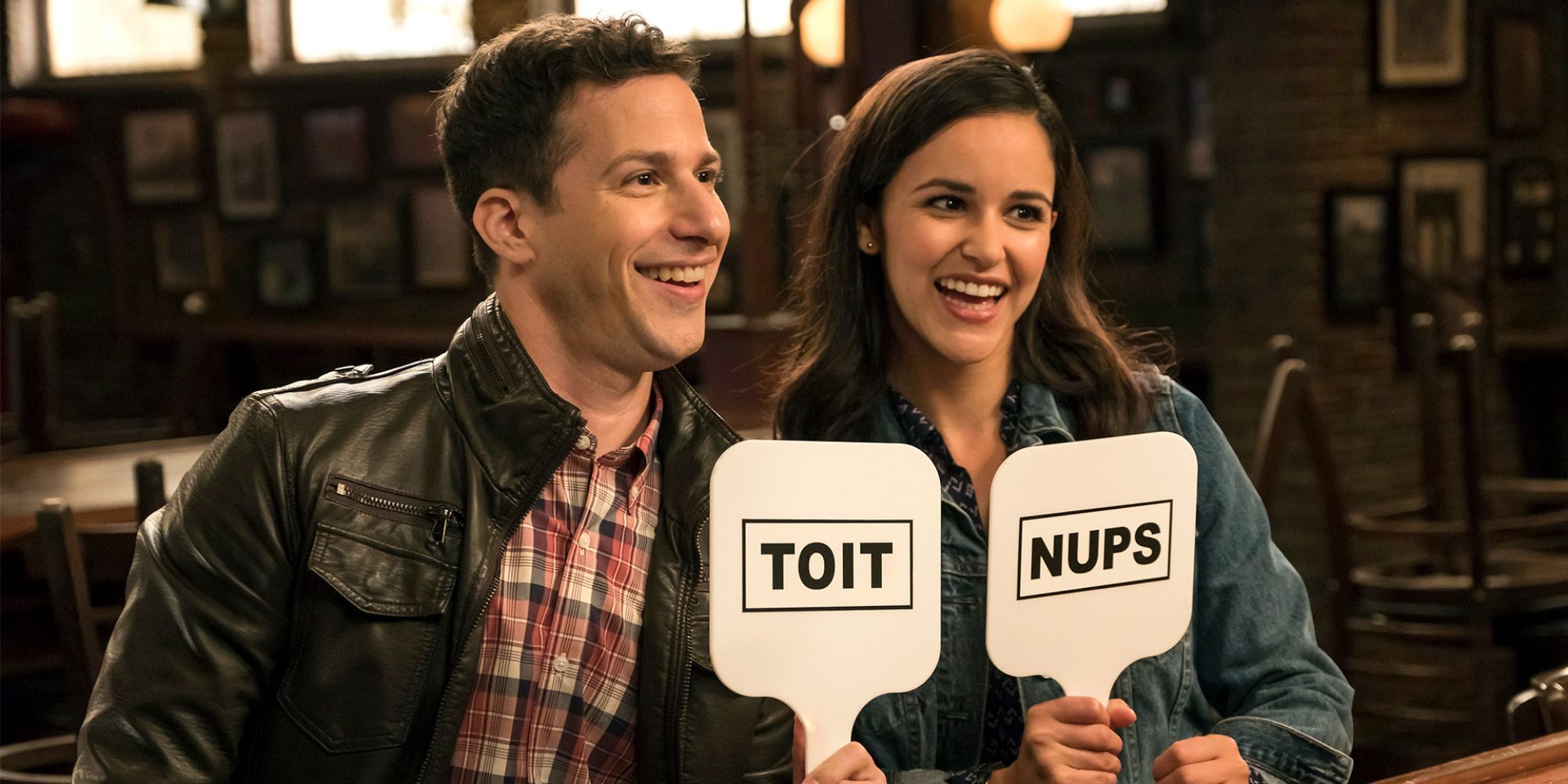 Jake et Amy sourient en tenant des pancartes à Brooklyn Nine-Nine.