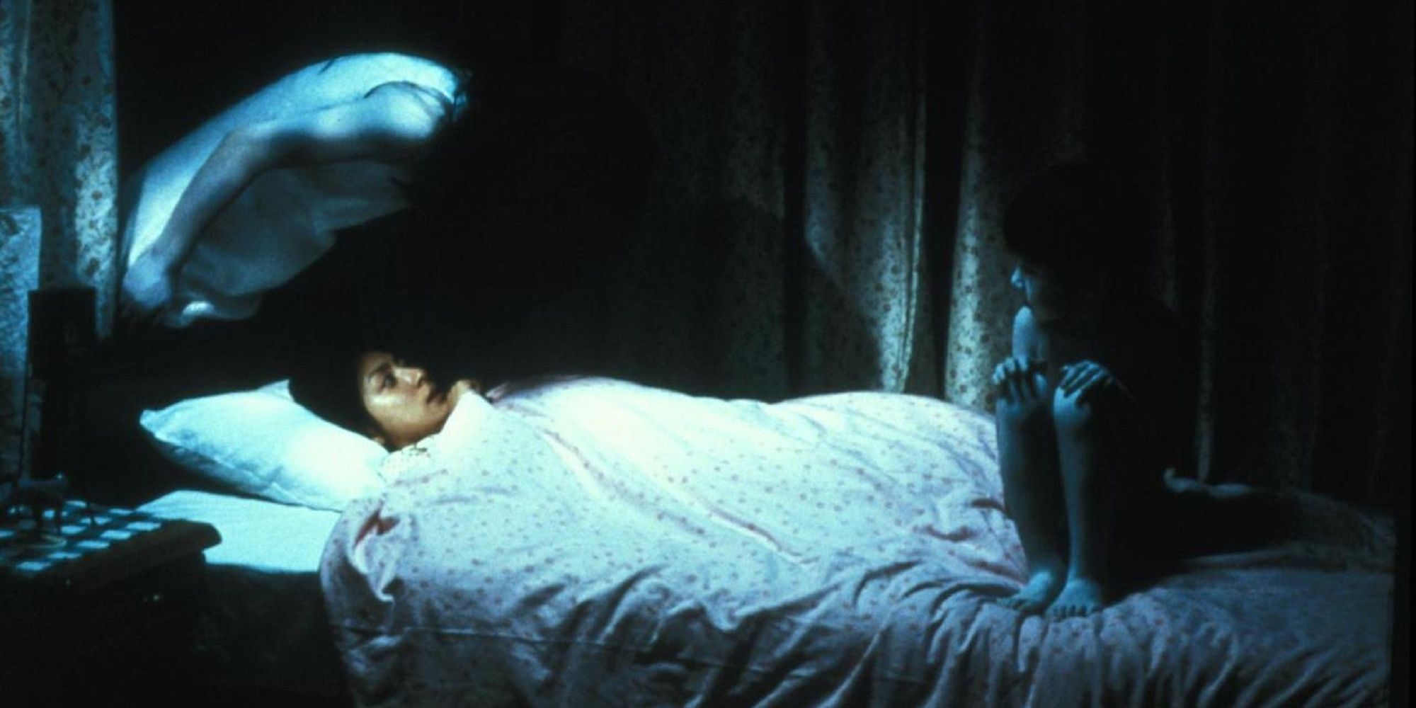 Paranormal entities sitting on the bed of Rika in 'Ju-on: The Grudge.'