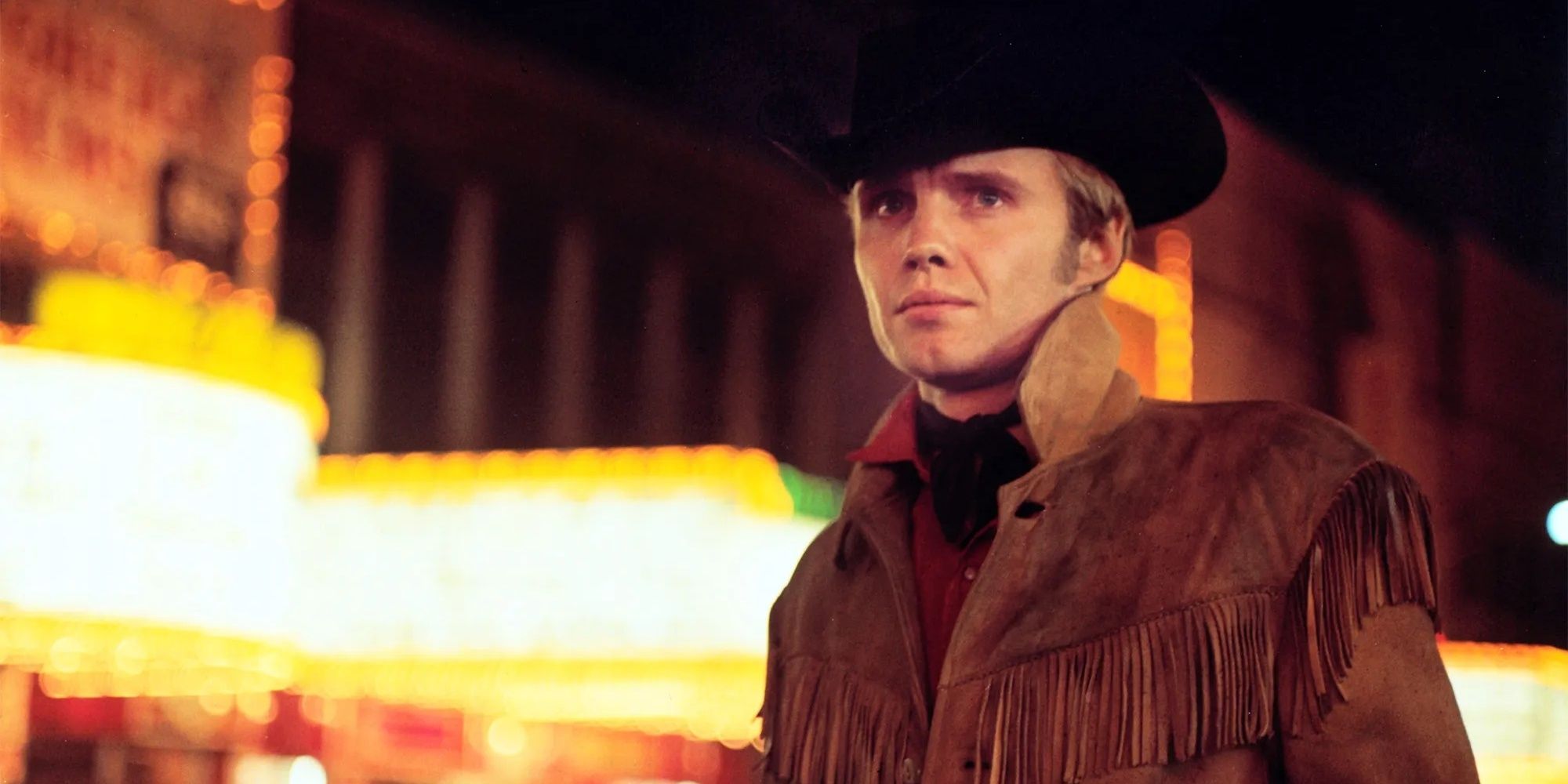 Jon Voight wearing a black cowboy hat under the New York City lights in 'Midnight Cowboy.'