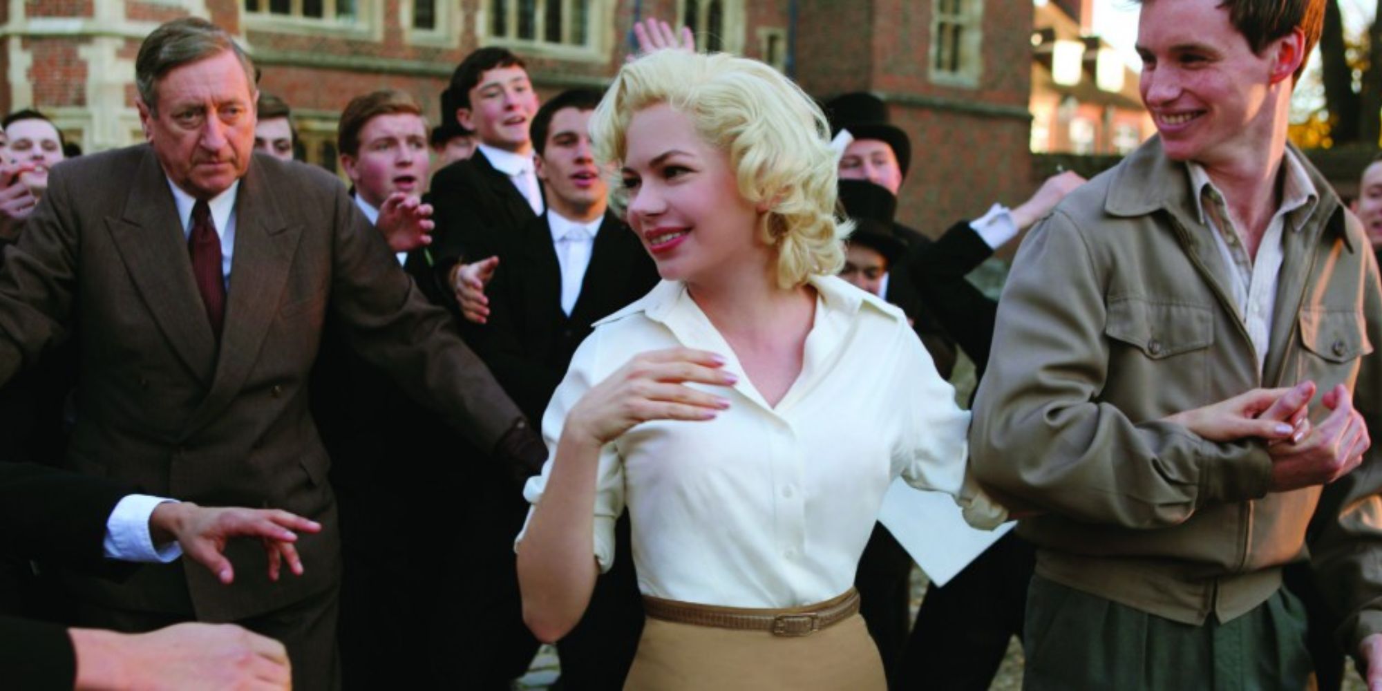 Marilyn Monroe smiling at a crowd while being scorted by a smiling man in My Week with Marilyn.