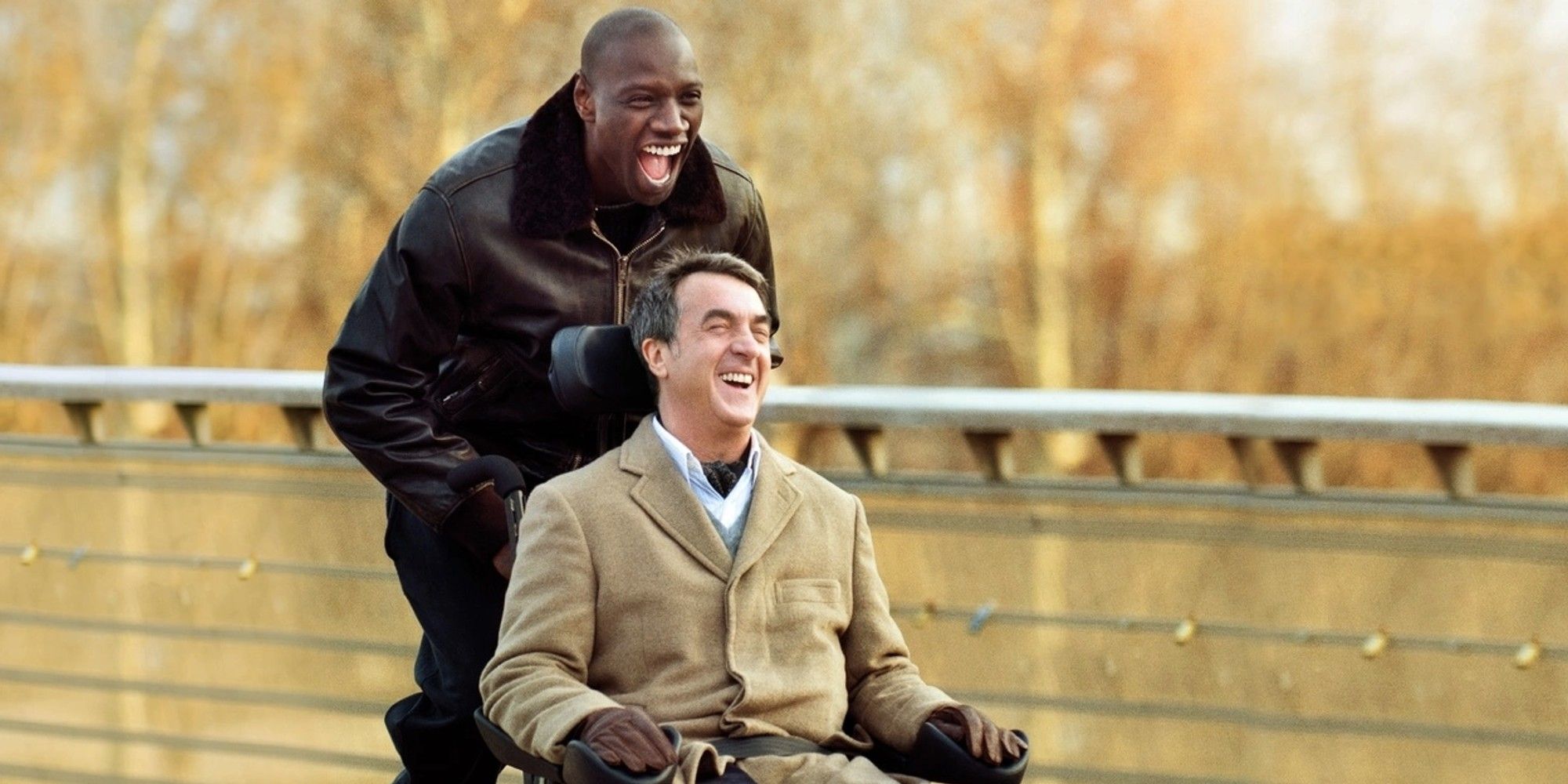 A man pushes another man in a wheelchair, both laughing, in The Intouchables.