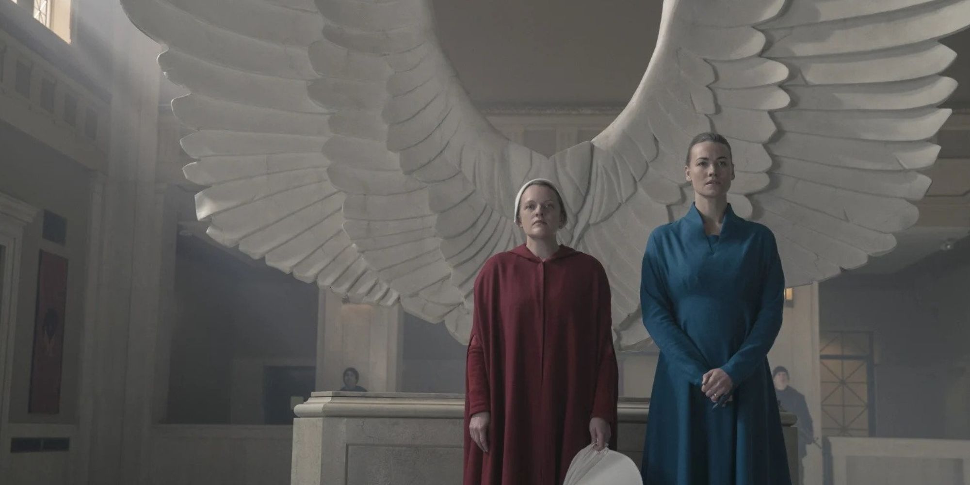 Serena and June standing in front of a statue of white wings
