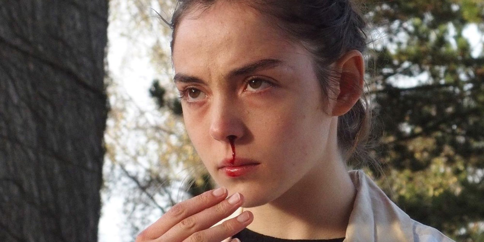 Still from 'Raw': Close up of Justine (Garance Marillier) glaring. She has a nosebleed. 