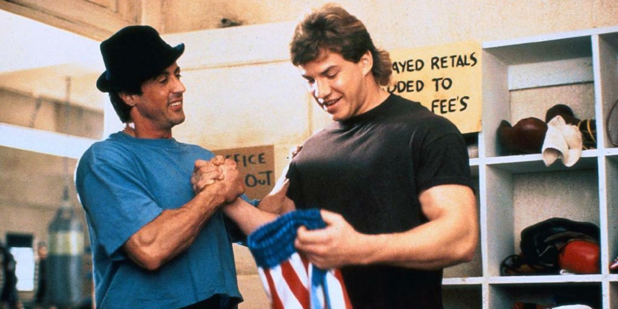 Sylvester Stallone and Tommy Morrison as Rocky and Tommy, smiling and shaking hands while Tommy holds a pair of wrestling shorts in Rocky V