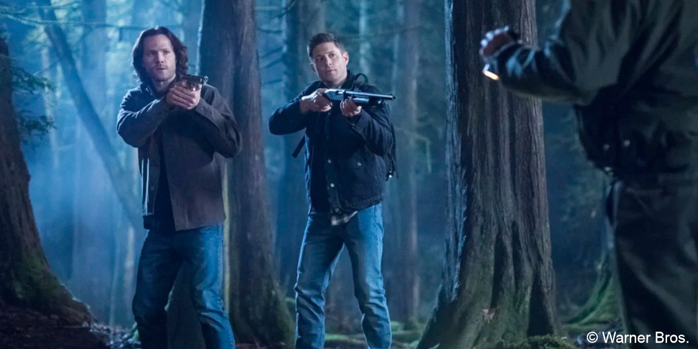 Jared Padalecki and Jensen Ackles stand in a forest pointing guns at a man in Supernatural