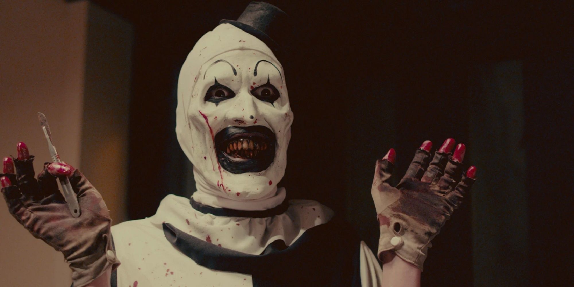 Art the Clown com um bisturi na mão enquanto sorri em 'Terrifier 2'.