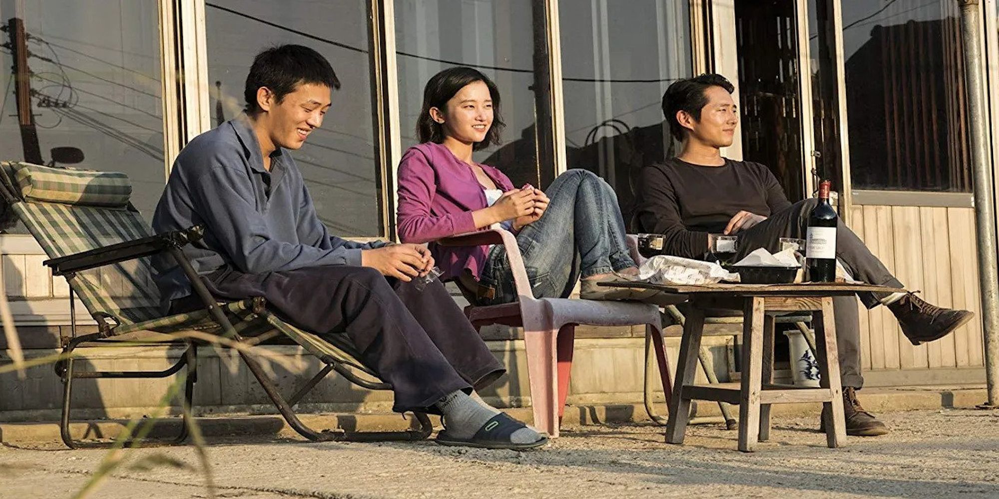 Two men and a woman sitting on the porch of a house in the film Burning.
