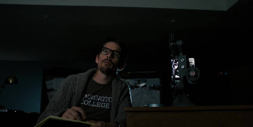 Ellison sitting next to a film projector looking ahead at a movie in Sinister.