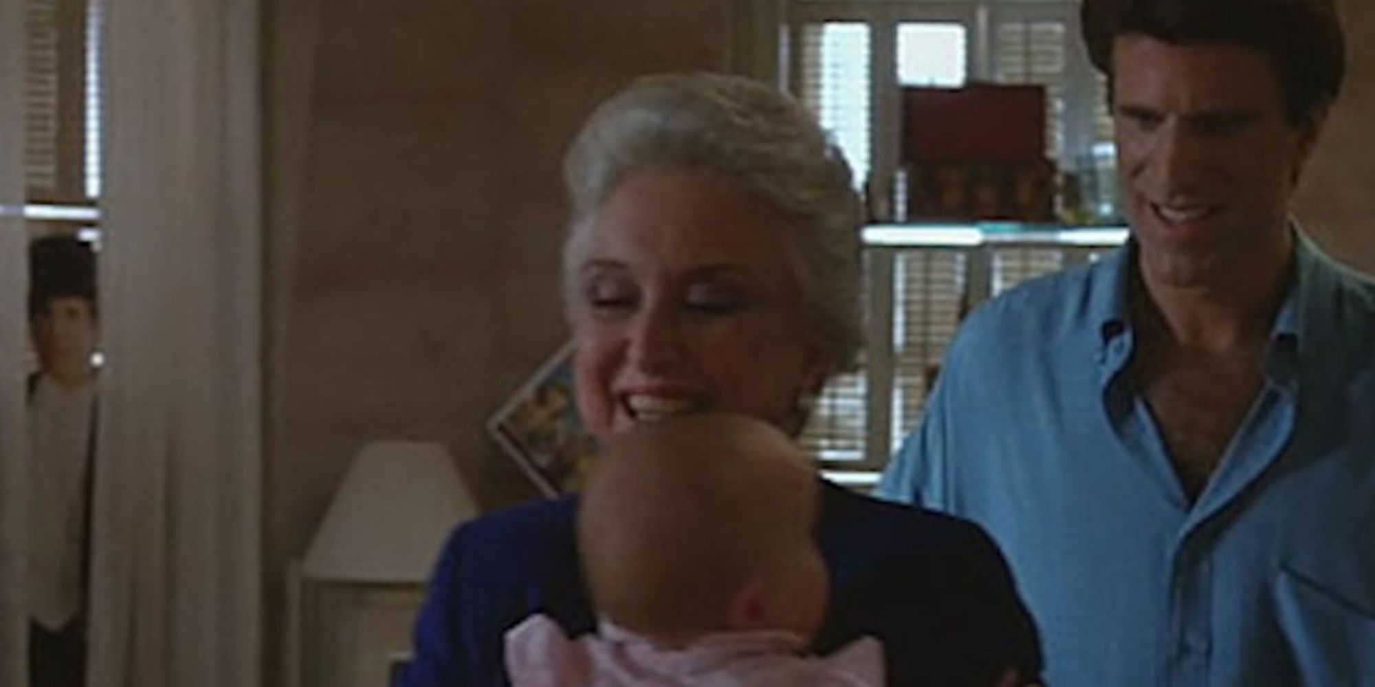 Parents carry their adored baby while a sinister figure lurks in the background, behind the curtains
