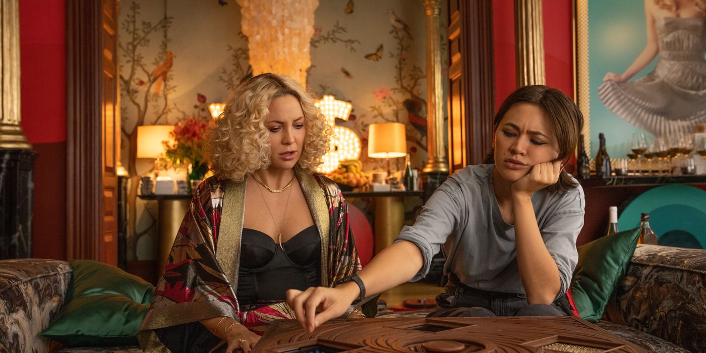 Kate Hudson as Birdie Jay and Jessica Henwick as Peg working on a puzzle box in Glass Onion: A Knives Out Mystery