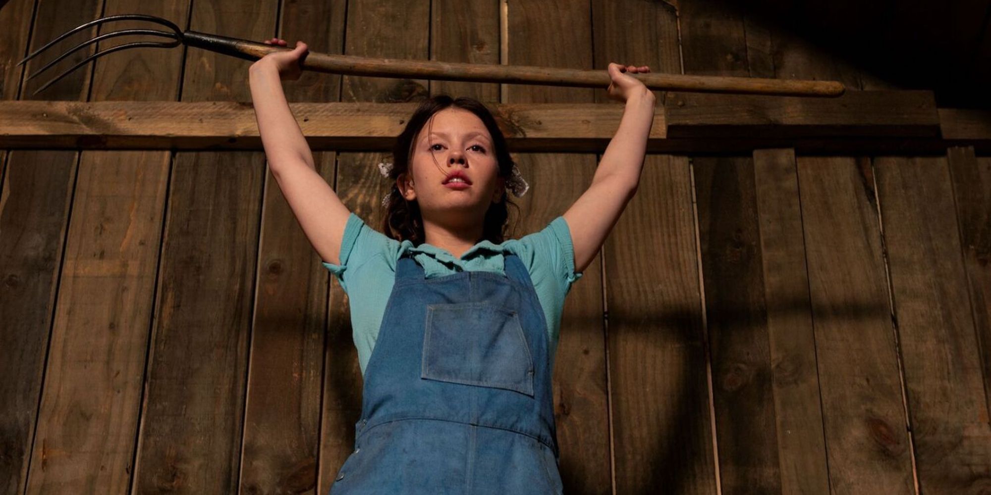 Pearl raises a pitchfork above her head in the film Pearl